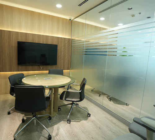 Small meeting room office fit-out by Blueprint Experts – glass-partitioned space with round table, chairs, and wall-mounted TV.