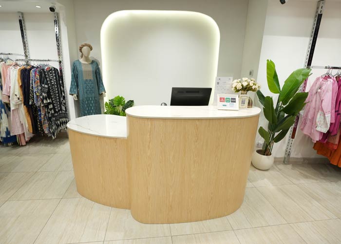 Reception desk fit-out – curved light-wood reception counter with white countertop and modern backlit wall panel.