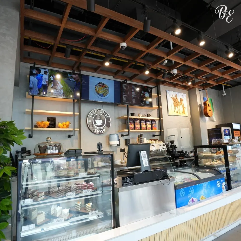 Contemporary cafe interior design with wood-accent ceiling and dessert display by Blueprint Experts