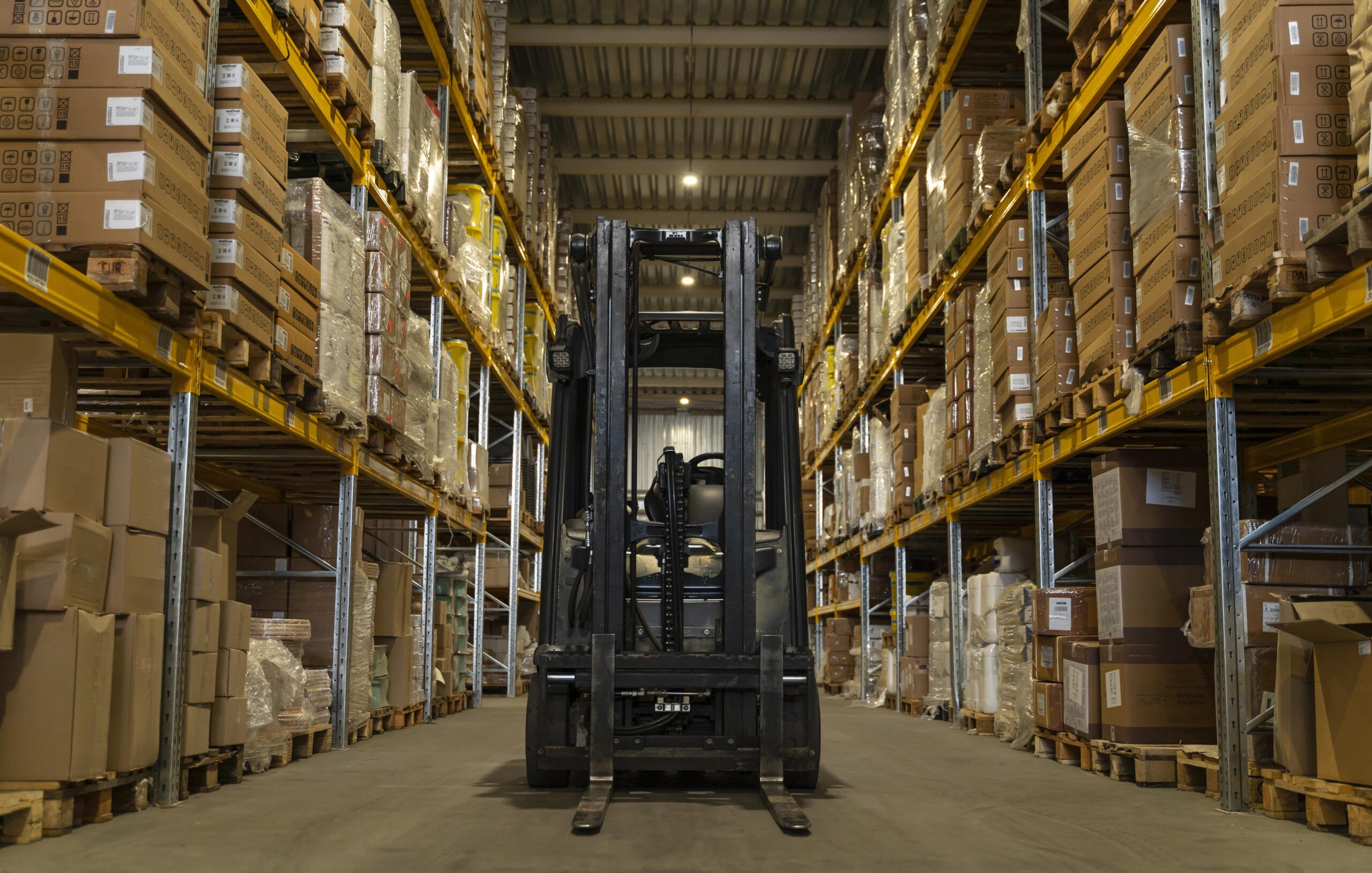 Warehouse logistics interior fit-out by Blueprint Experts – organized storage facility with pallet racking, stacked cartons, and a forklift operating in a wide central aisle.